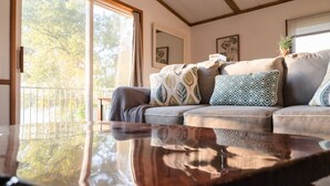 A living room with a glass coffee table, a grey sofa with patterned cushions, and a balcony with a railing. - Serene 3-Bedroom Getaway with Stunning Lake Views (Aberdeen)