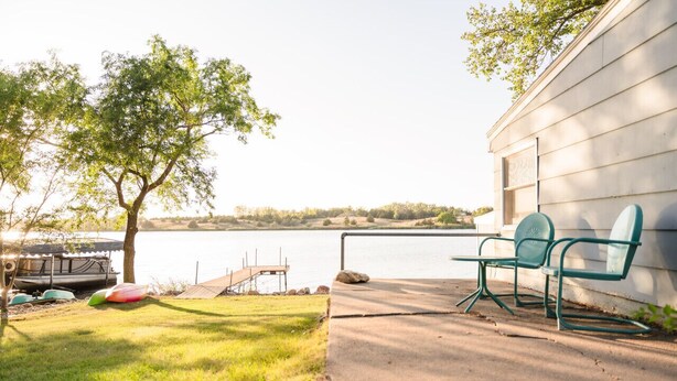 A lakeside patio with a concrete deck, two green chairs, a small dock, and a boat. - Serene 3-Bedroom Getaway with Stunning Lake Views (Aberdeen)