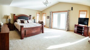A spacious bedroom with a large bed, a television, and a sliding glass door to the outside. - The Lakeside Retreat (Aberdeen)