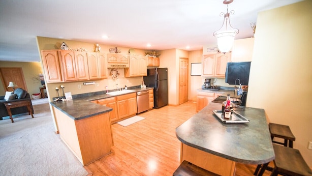 A kitchen with wooden cabinets, a central island, and a dining area with a bar stool. - The Lakeside Retreat (Aberdeen)