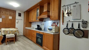 Una cocina compacta con armarios de madera, una mesa de comedor con mantel floral y un calendario colgado en la pared.