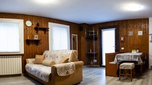 Una sala de estar acogedora con un sofá, una mesa de comedor con sillas, paredes de madera y un radiador.