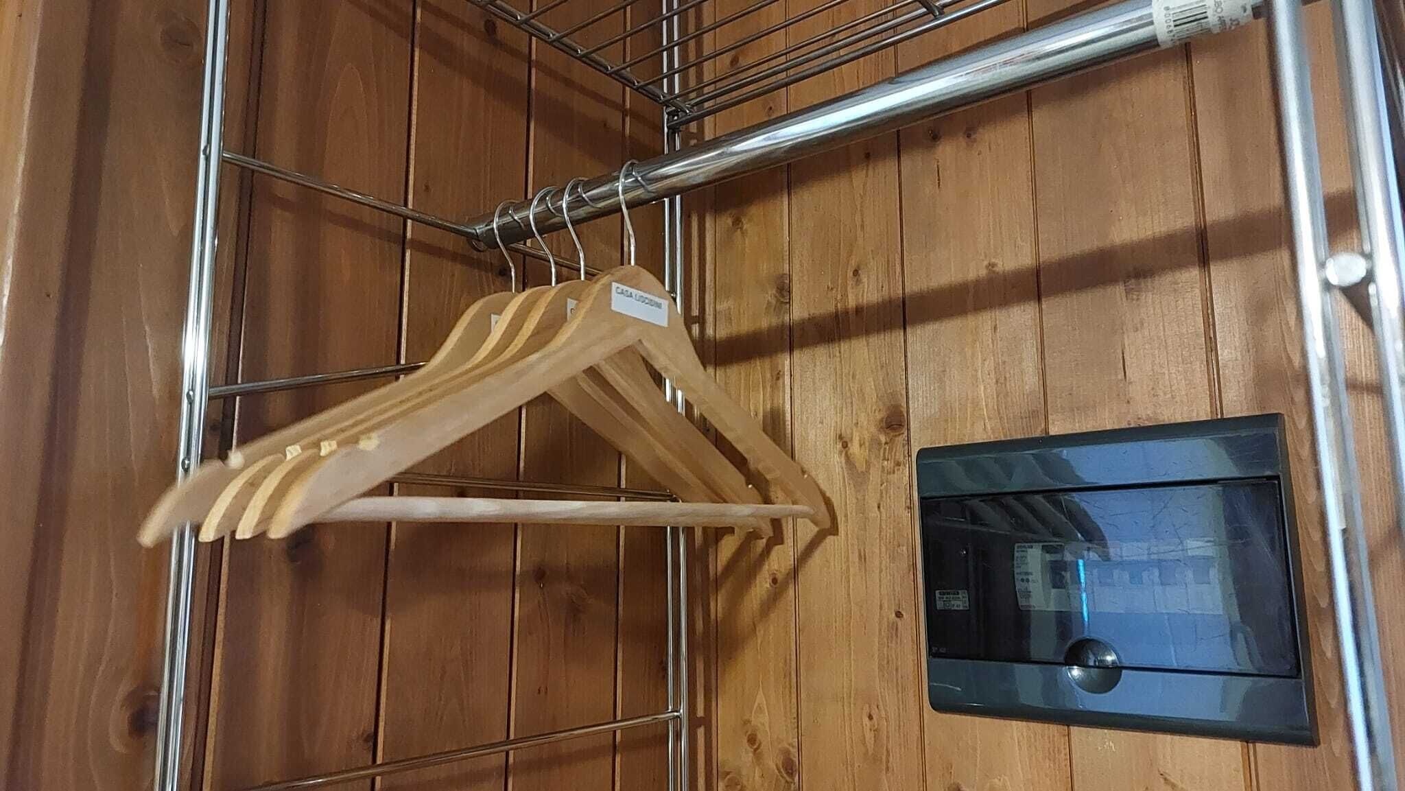 Una pared de madera con un perchero metálico que sostiene perchas de madera y un termostato negro.