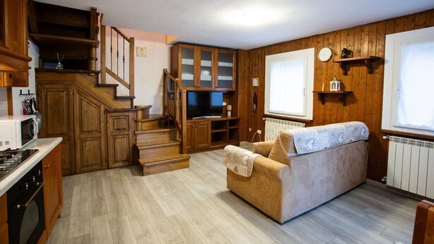 A compact living space with a kitchen, a sofa, a TV, and a staircase leading to a loft area. - Liscidini House Holidays in Aprica (Aprica)