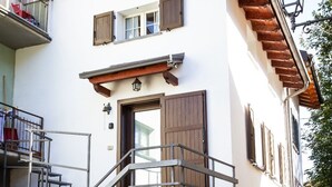 Un edificio de dos pisos con base de piedra, una escalera de madera con barandillas de metal y un balcón con baranda metálica.