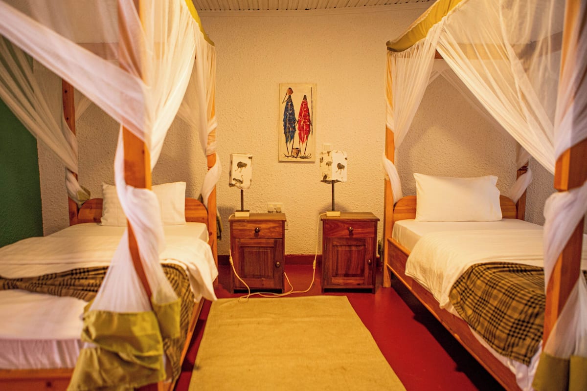 A room with two beds, each with a canopy, wooden nightstands, and a painting on the wall.