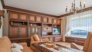 Ein Wohnzimmer mit einem großen Holzkabinett, einem Fernseher und einer Kristallleuchtre.
