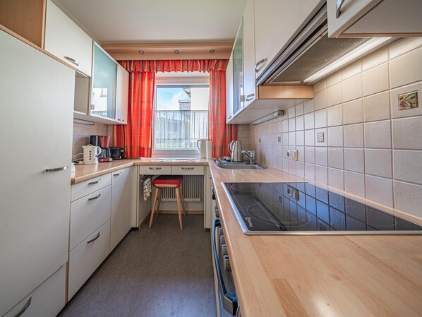 Cocina compacta con estufa integrada, un lavamanos y una ventana con cortinas rojas.