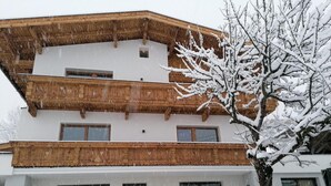 Ein mehrgeschossiges Gebäude mit hölzernen Balkonen und einem schneebedeckten Baum davor.