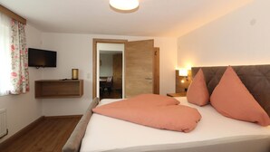Ein Schlafzimmer mit einem Bett, einem Fernseher, einem Holzregal und einer Tür zu einem anderen Raum.