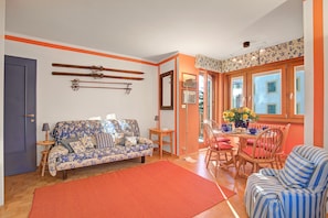 A living room with a sofa, a dining table with chairs, and a red rug. - Appartamento Fraiteve Ski In Ski Out 300m (Sestriere)