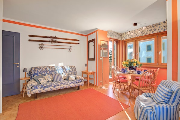 A living room with a sofa, a dining table with chairs, and a red rug.
