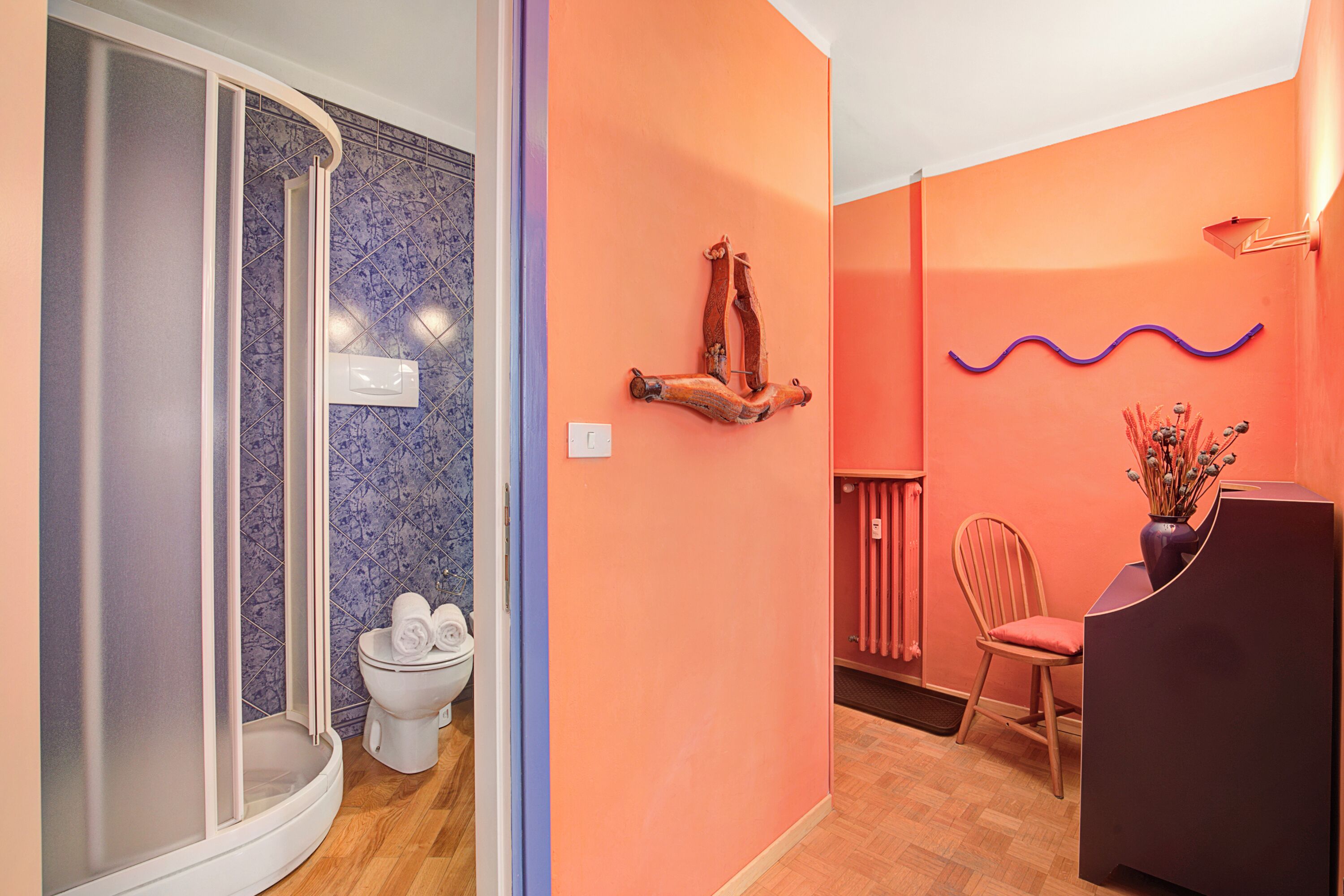 Ein Badezimmer mit Dusche, Toilette und Waschtischbereich mit Stuhl und Blumenvase.