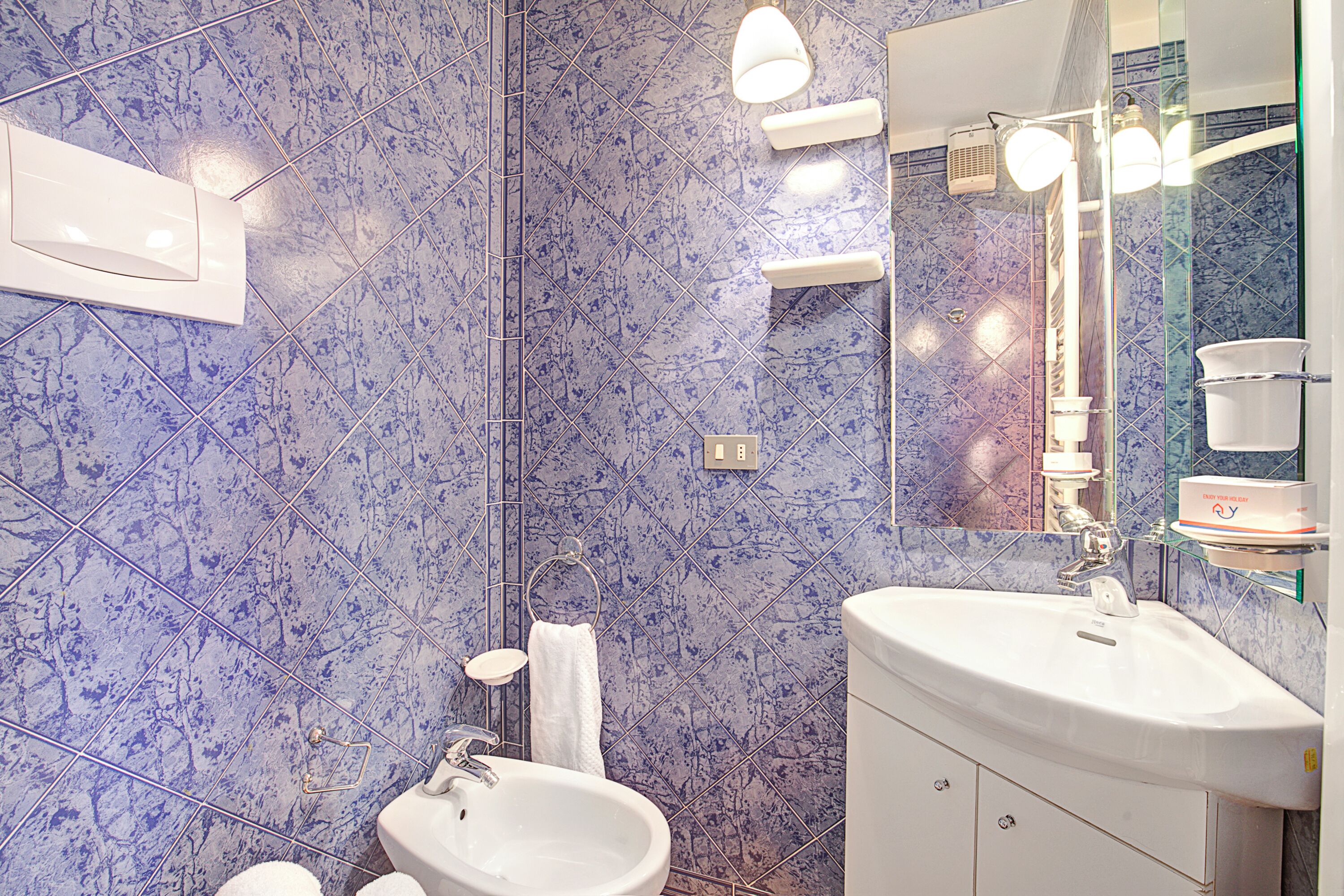 Ein Badezimmer mit weißem Waschbecken, Spiegel und blauen Fliesen.