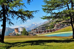 A mountainous resort with buildings, a lake, and snow-capped peaks in the background.