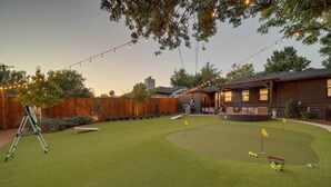 Een achtertuin met kunstgras, een putting green en een houten omheining.