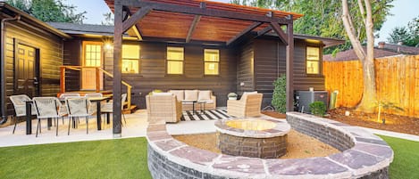 A backyard with a stone fire pit, outdoor furniture, and a pergola.