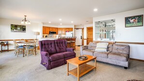 Ein Wohnzimmer mit einem violetten Sofa, einem braunen Sofa, einem Holztisch und einem Essbereich mit Tisch und Stühlen.