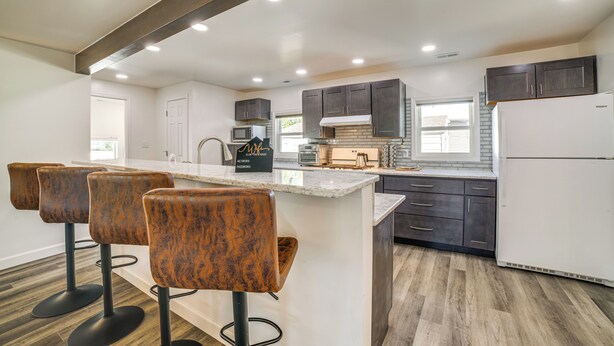 A modern kitchen with a central island, bar stools, dark cabinets, and a refrigerator. - < 1 Mi to Dwtn: Valparaiso Family Home (Valparaiso)