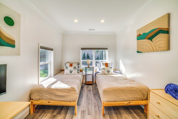 A bedroom with two beds, a window, and artwork on the walls.