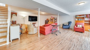 Een ruime woonkamer met een houten vloer, een rode bank, een blauwe fauteuil en een boekenkast.