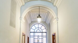 A hallway with a high ceiling, a large arched window, and a hanging light fixture.