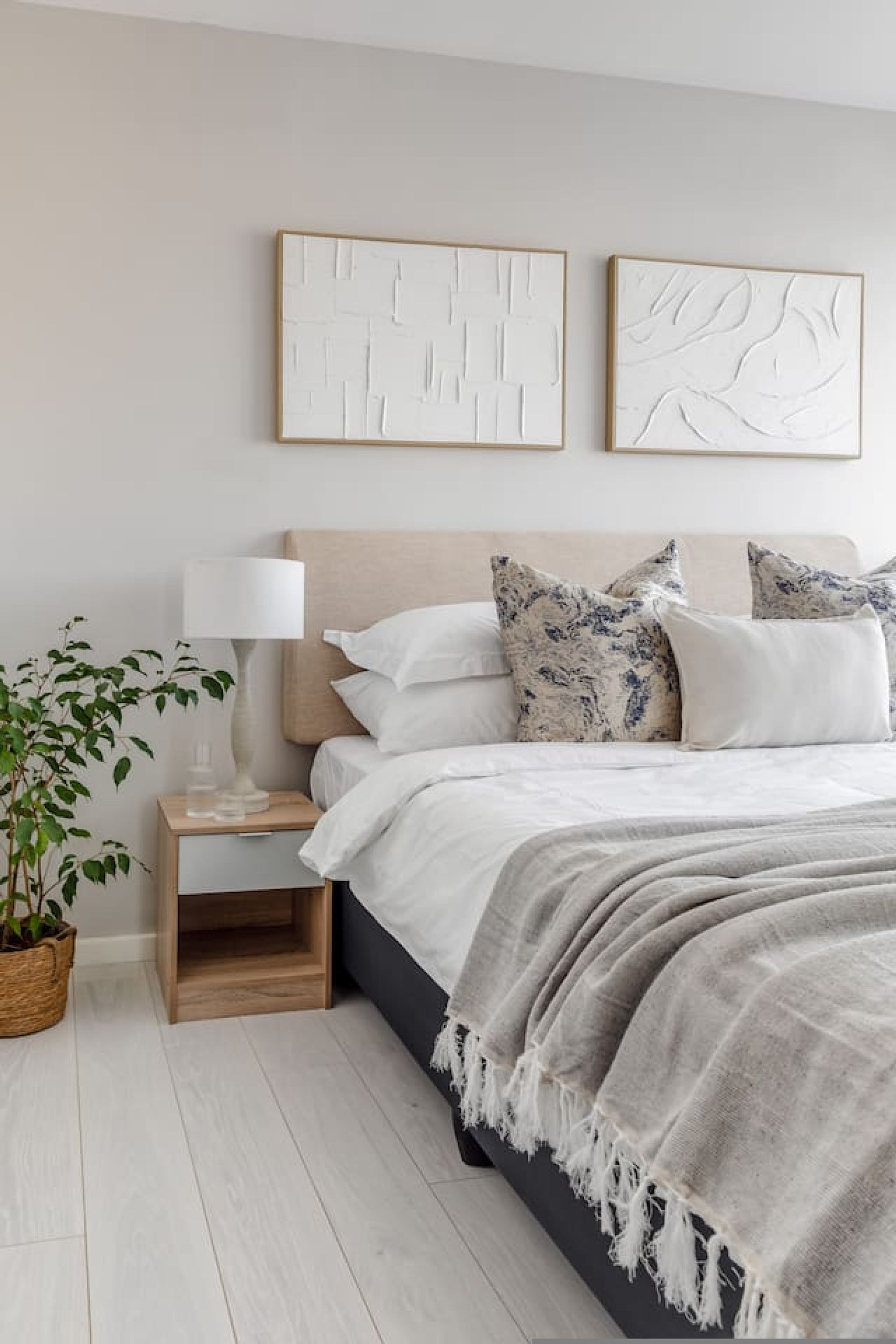 A bedroom with a bed, bedside table, lamp, and wall art.