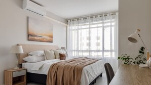 Ein Schlafzimmer mit Bett, Nachttisch, Lampe und Blick ins Freie durch ein Fenster.