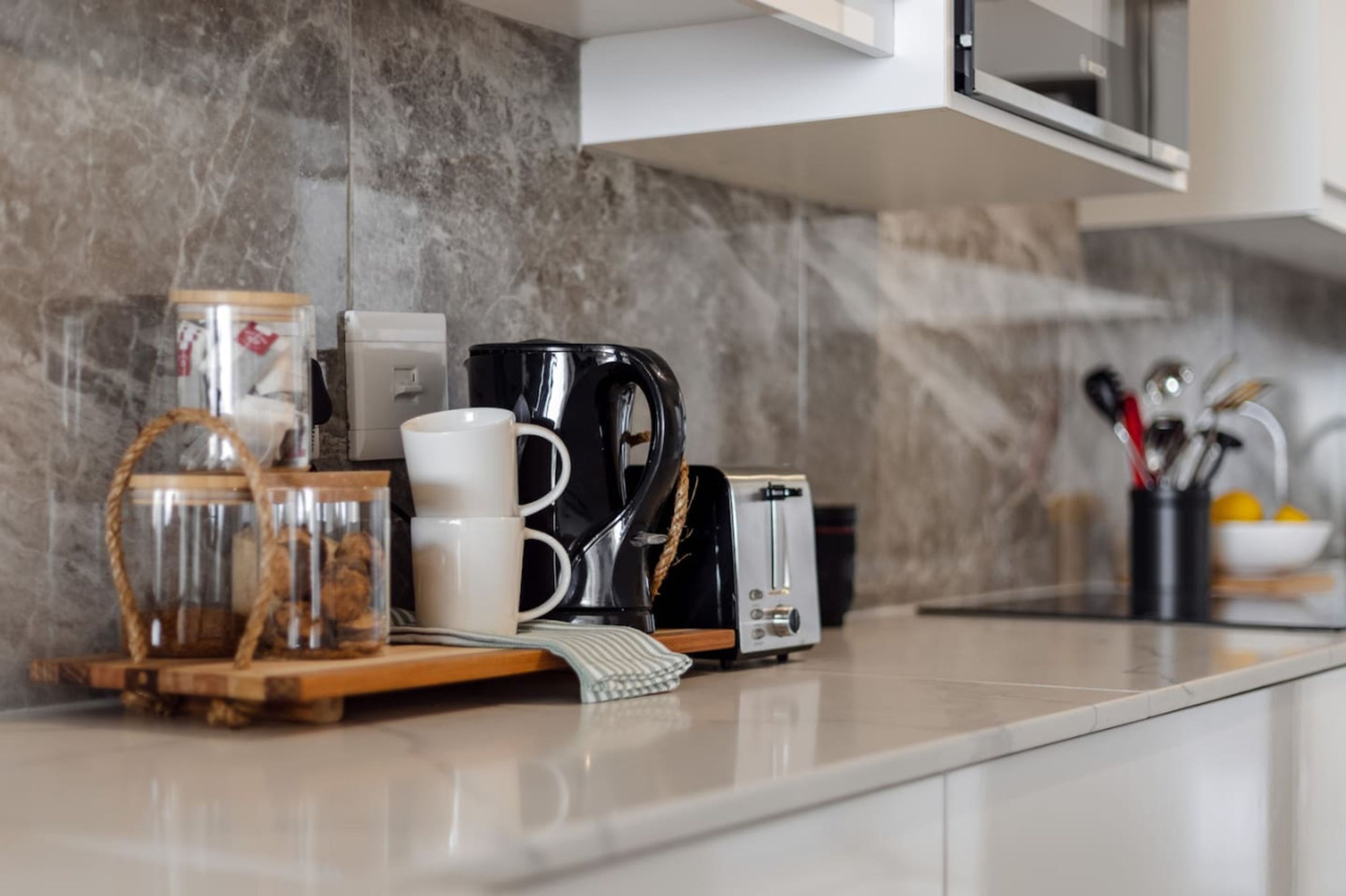 Un piano di lavoro in cucina con una macchina del caffè, un tostapane, una tazza bianca e un barattolo di vetro.