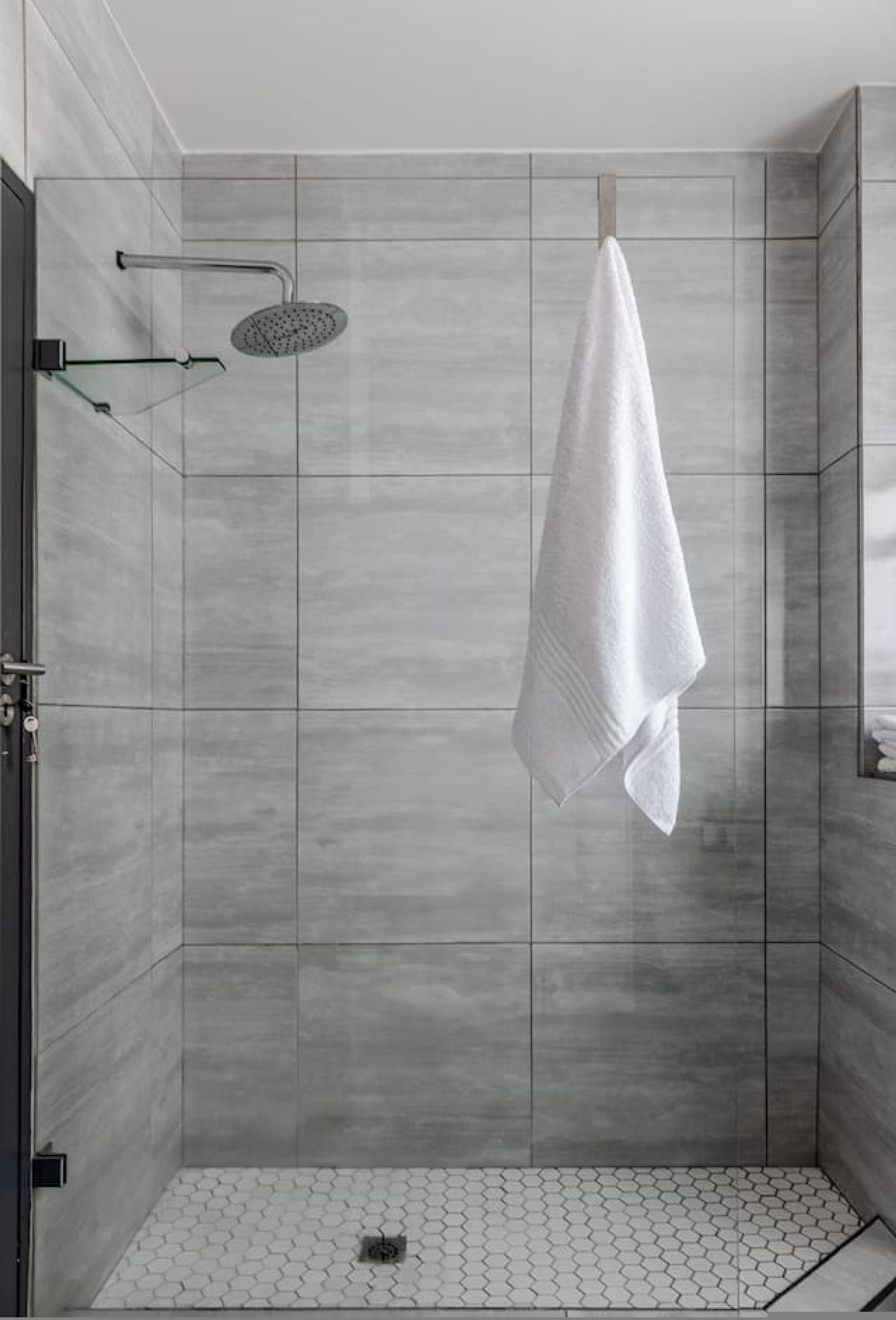 A modern shower with a rain showerhead, a towel hanging on a rack, and a tiled floor.