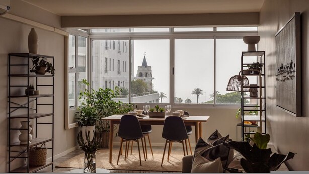 Ein Essbereich mit Tisch für zwei Personen, großen Fenstern und Blick auf ein Gebäude.