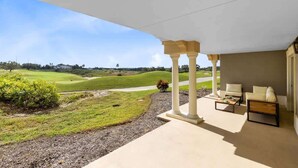 A covered outdoor area with a view of a golf course, featuring a seating arrangement and a pergola structure.