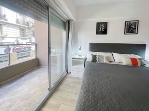 Relax in a spacious room with a large bed, bedside table, and sliding glass door leading to a balcony with a city view.