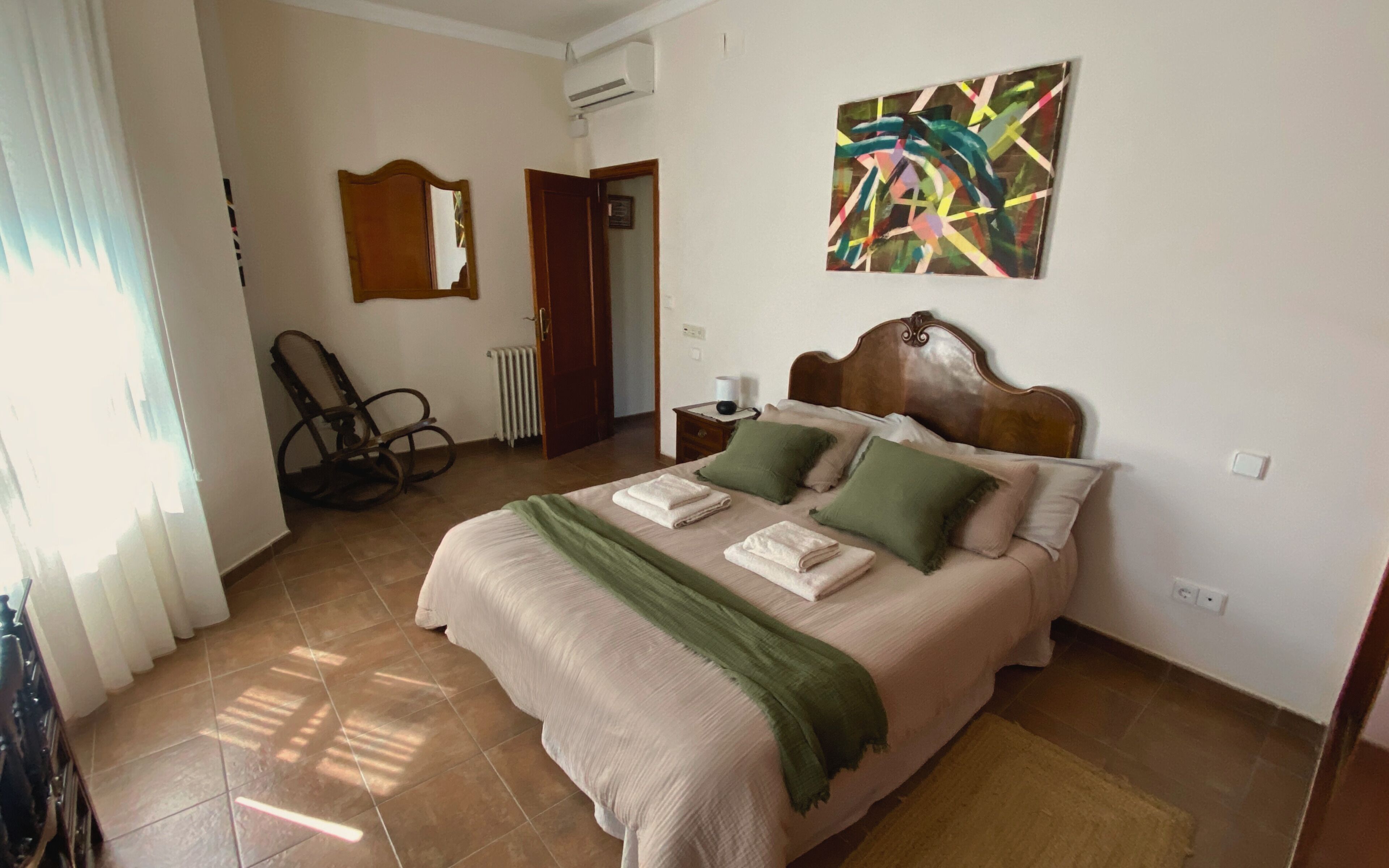 Ein Schlafzimmer mit Bett, Kissen, einem Sessel, einem Heizkörper und einem Bild an der Wand.