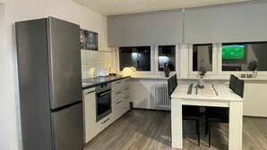 A modern kitchen with a refrigerator, oven, and a dining area with a table and chairs. - Stylish apartment in the middle of the Ruhr area (Bochum)