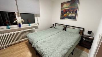 Ein Schlafzimmer mit einem Bett, einem Heizkörper, einem Fenster mit Blick, einem Bild an der Wand und einem Nachttisch mit Lampe.