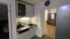 A compact kitchen with white cabinets, a coffee maker, a sink, and a clock on the wall. - Stylish apartment in the middle of the Ruhr area (Bochum)