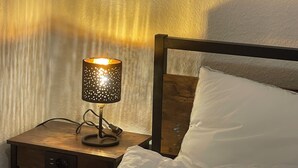 A bed with white bedding, a wooden nightstand with a lamp, and a wall with a textured pattern. - Stylish apartment in the middle of the Ruhr area (Bochum)