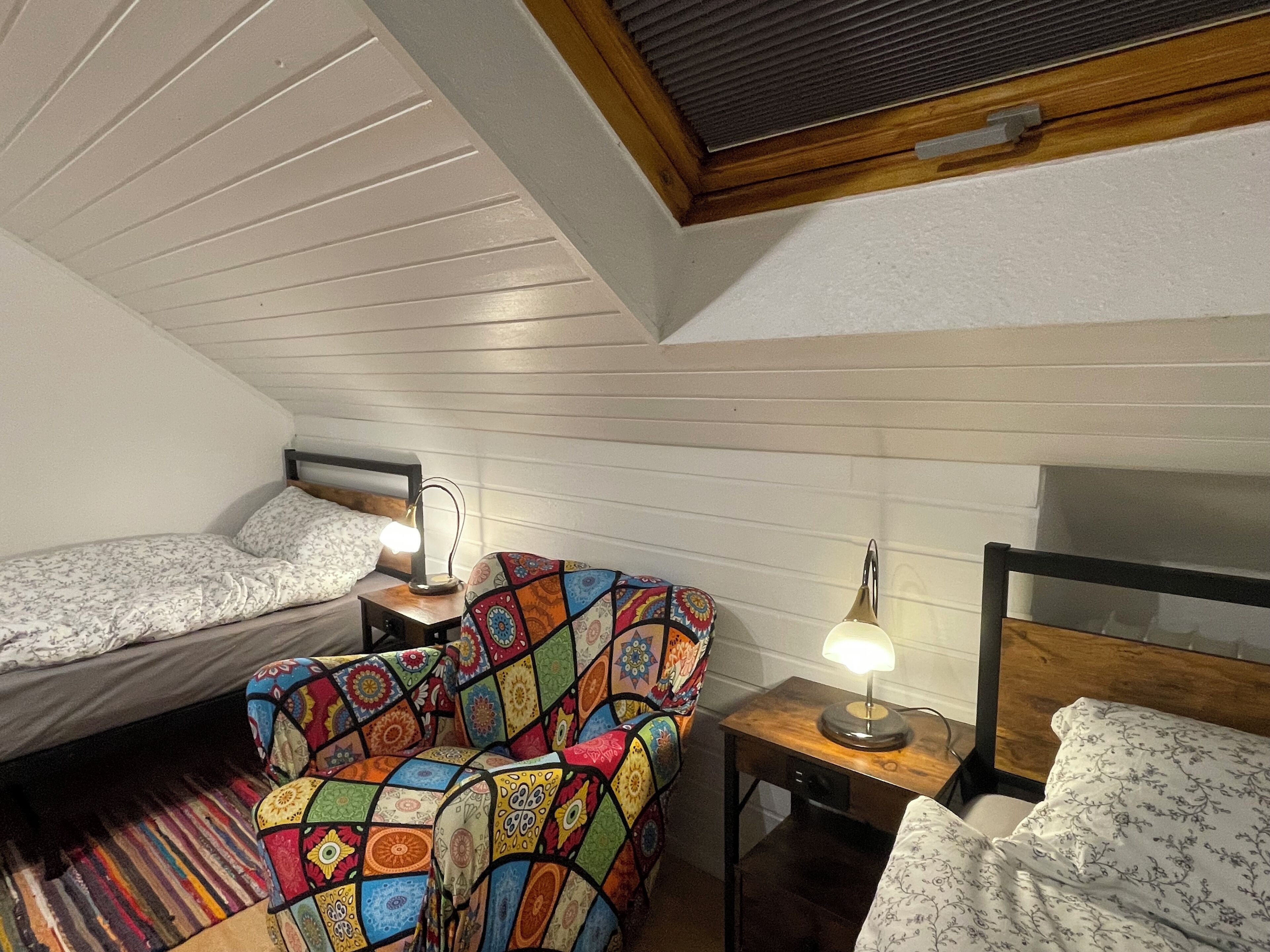 Une petite pièce accueillante avec deux lits, une courtepointe aux couleurs vives, une tête de lit en bois et une petite table avec une lampe.