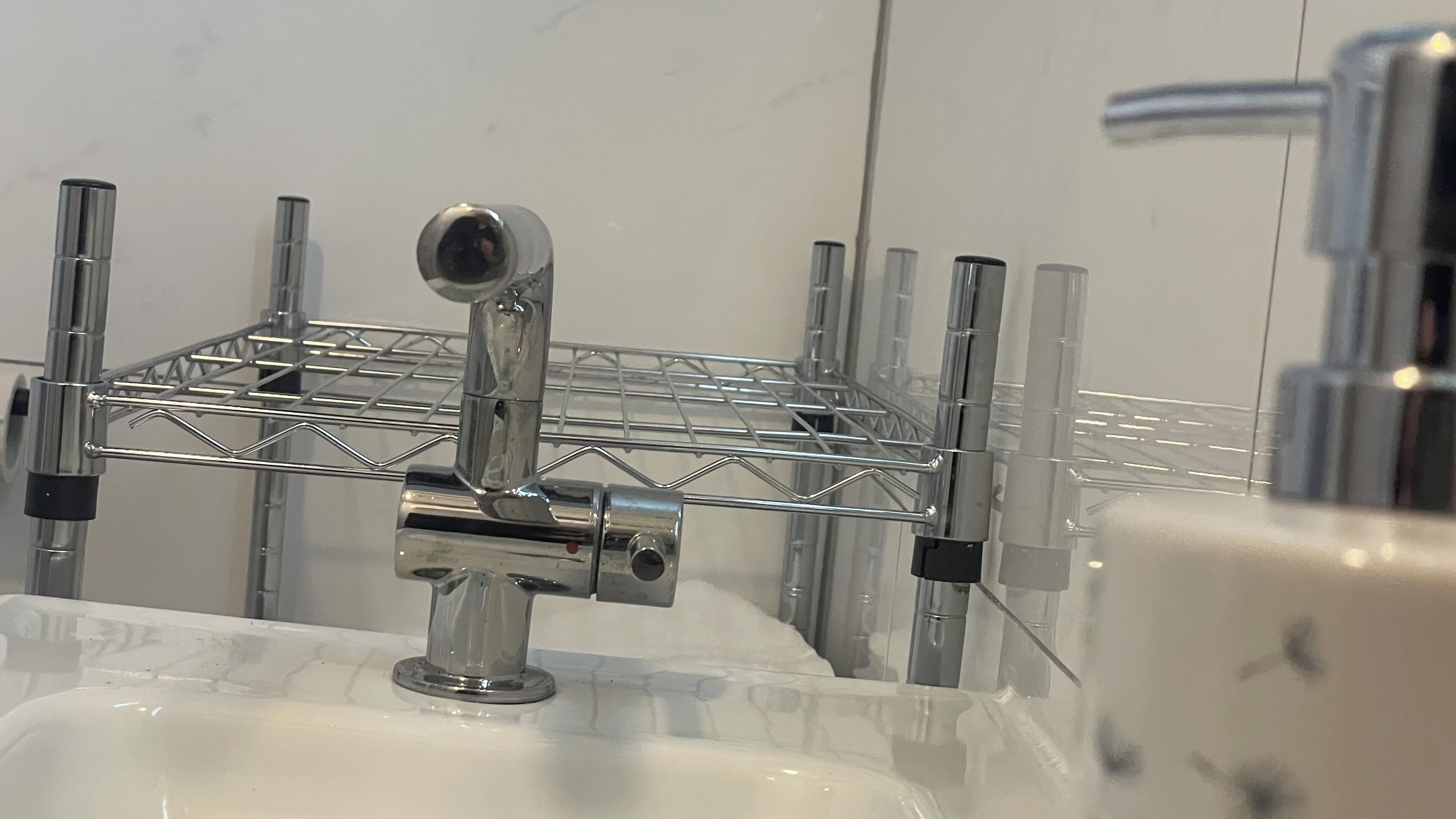 A bathroom with a chrome faucet, a mirror, and a metal rack with toiletries.