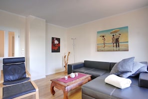 A living room with a sofa, a chair, a coffee table, and artwork on the walls. - Strandvilla Börgerende - Vacation Apartment 4 (Börgerende)