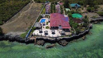 Vista aérea de una propiedad costera con piscina, varias construcciones y un litoral rocoso.