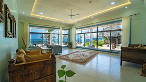 Un salón amplio con un gran ventanal con vista al océano, un ventilador de techo y un sofá de madera.
