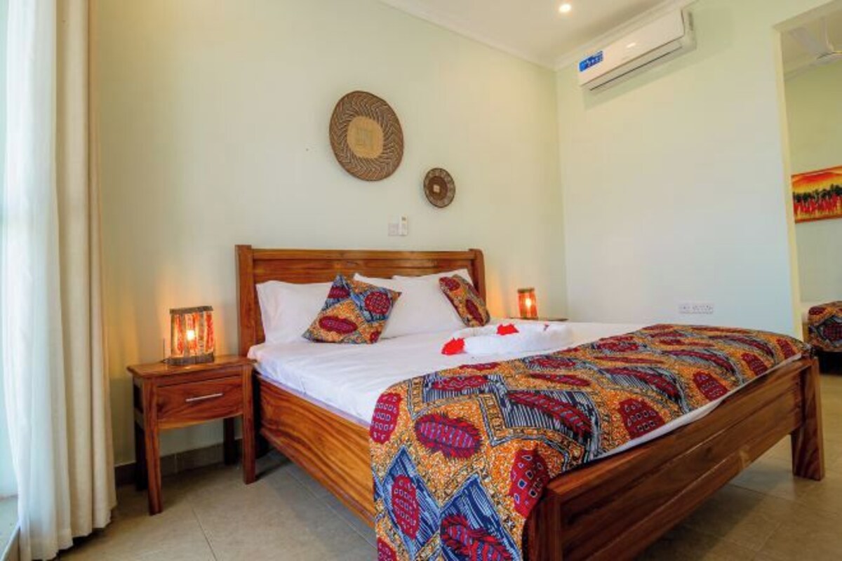 Quarto com cama de madeira, luminárias de cabeceira, ar condicionado fixado na parede e um adorno pendurado na parede.