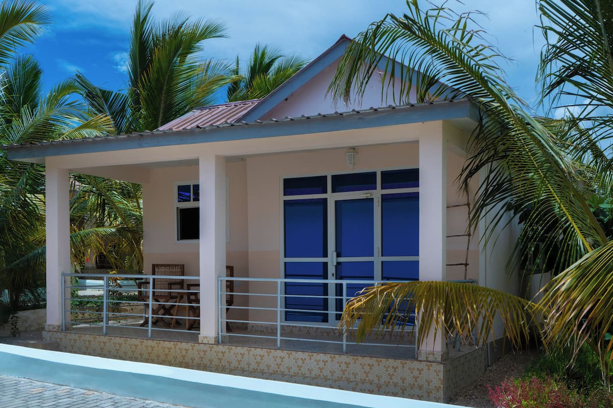 A small, single-story building with a covered patio area, a pool, and surrounded by palm trees.