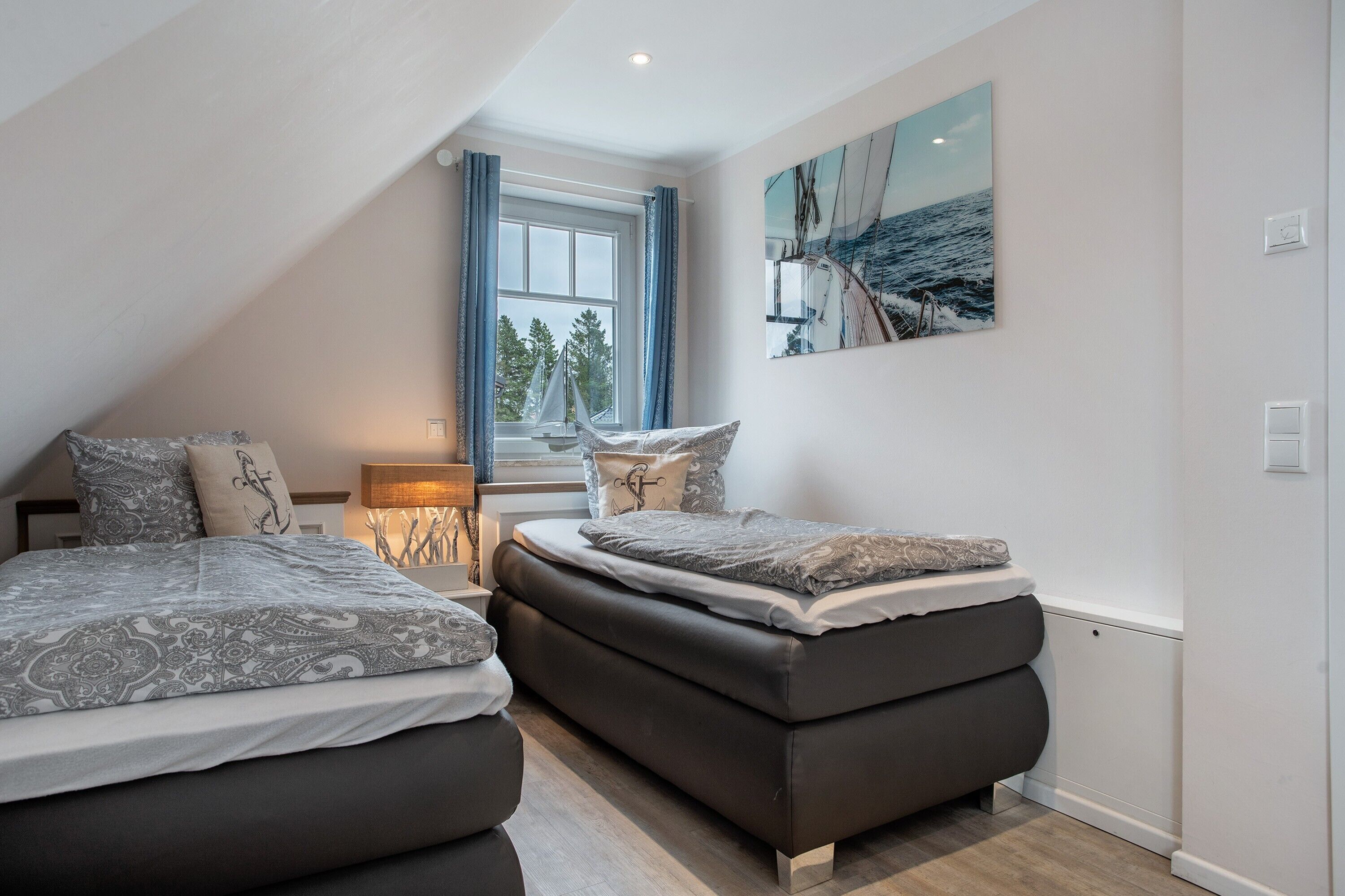 A bedroom with two beds, a window with curtains, a painting, and a lamp.
