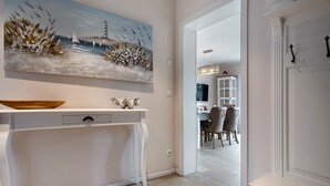 Un interior moderno con una zona de comedor, un cuadro de una escena costera y una consola blanca.
