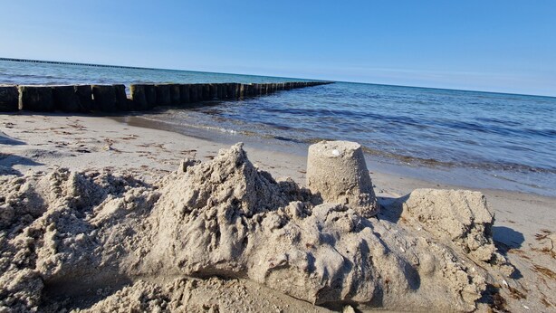 Una playa arenosa con una estructura de hormigón y un cielo azul despejado.
