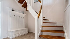 Una escalera con peldaños de madera y barandillas blancas, un banco blanco con ganchos y un suelo de madera claro.