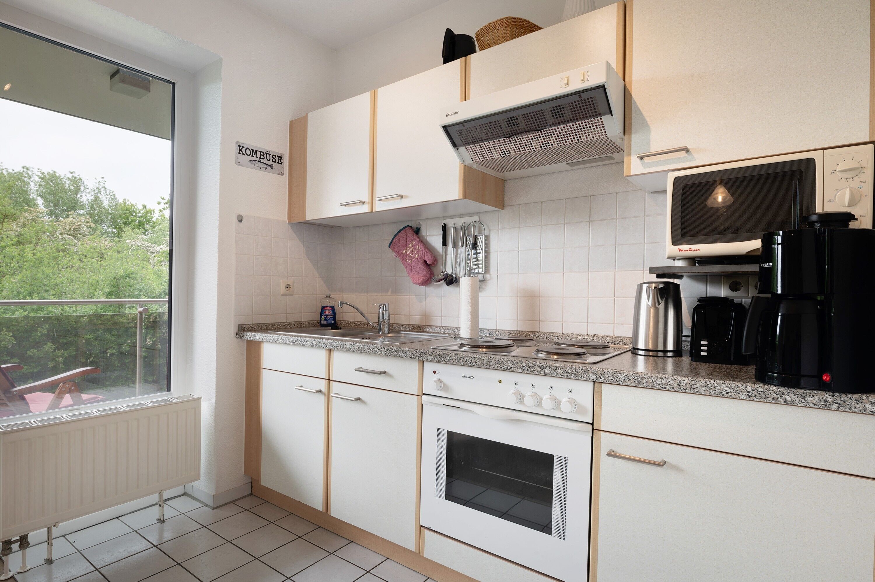 Una cocina moderna con armarios blancos, horno empotrado, microondas y hervidor.